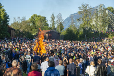 Sankthansbålet brenner midt på en slette fylt med glade tilskuere, de gamle husene på Hedmarkstunet og Hamardomen vises i bakgrunnen. (Foto/Photo)