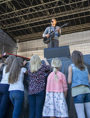 En ung gitarist i dongerijakke står på scenen, små jenter står foran og ser opp på ham. (Foto/Photo)