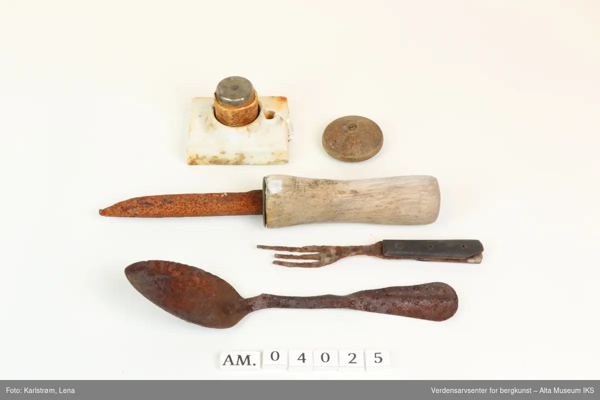 Samling husgeråd funnet ved Nordlysobservatoriet på Haldde: Kniv og gaffel med trehåndtak, metallskje, sikring i porselen og metall, lite rundt trobjekt.