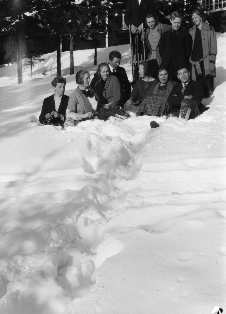 Gruppebilde av ti personer i dyp snø foran en større bygning