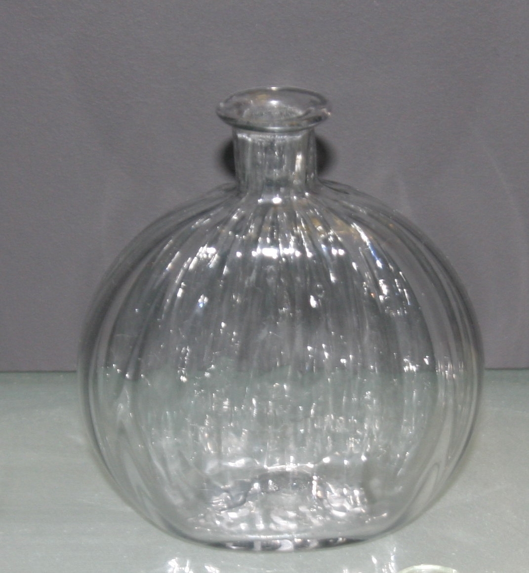 Liten, rund, flattrykt flaske i glass med vertikale striper preget i glasset.