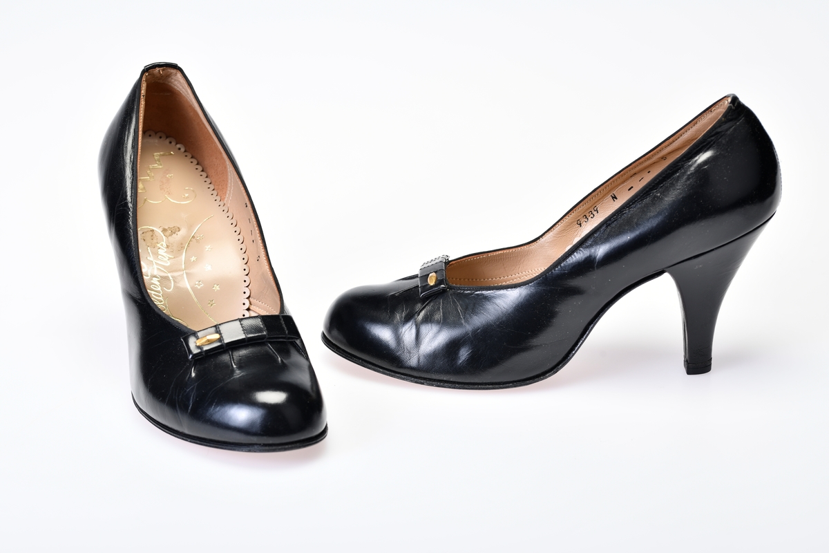 Sorte høghælte sko med dekor på oversiden. Foret. Tekst på innvendig såle og under skoen.