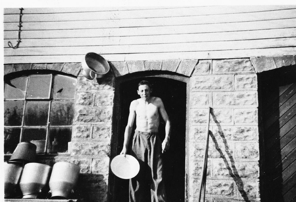 Mann med vaskefat i brunnhusdøra på Løge. Mjølkespanna til venstre og silen hengande på veggen.