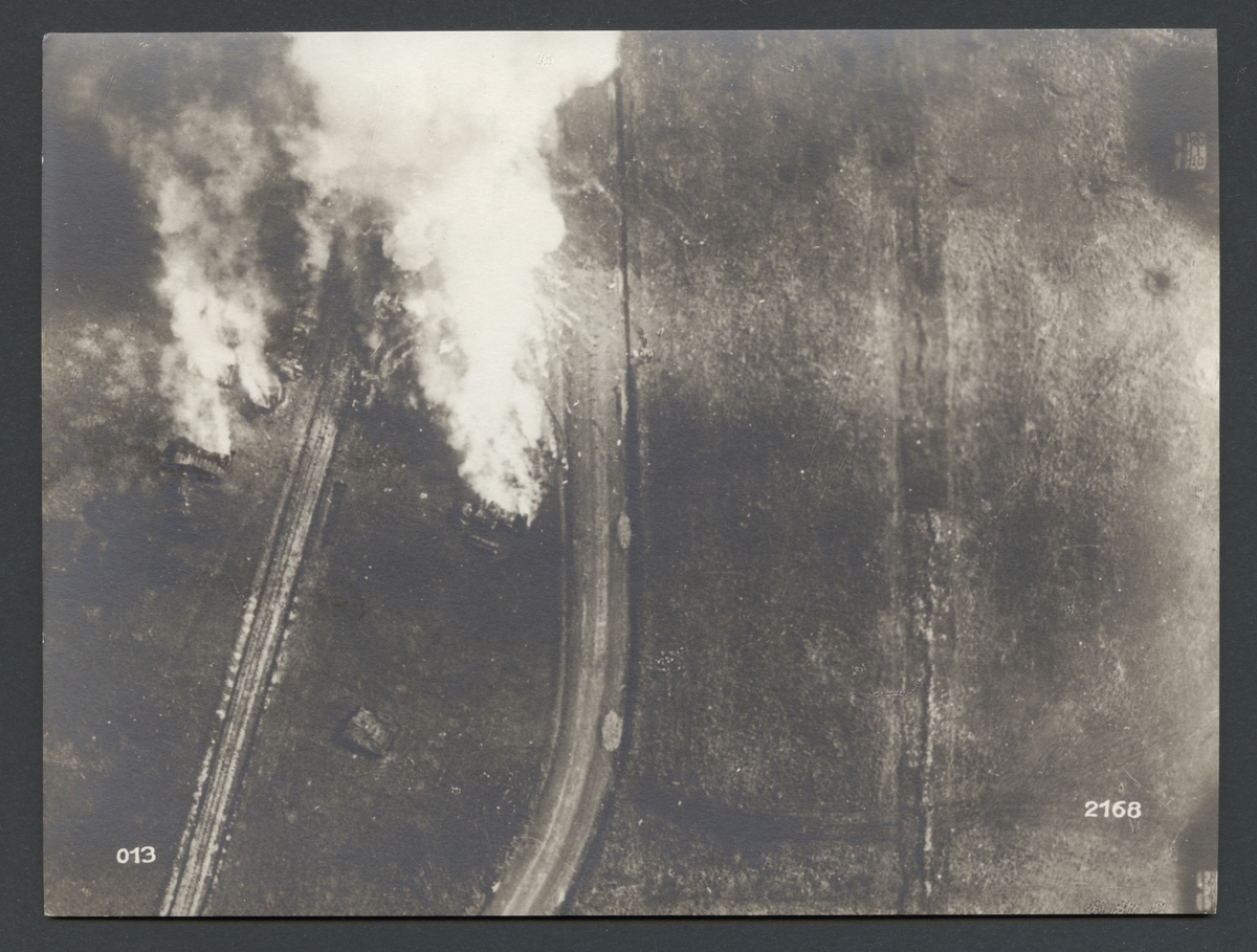 Denna flygbild visar brinnande föremål och rökmoln mellan en järnväg och en landsväg.

Originaltext: "Ett engelskt ammunitionsupplag, som skjutits i brand av tyskt artilleri. Fotografi taget av en tysk spaningsflygare."