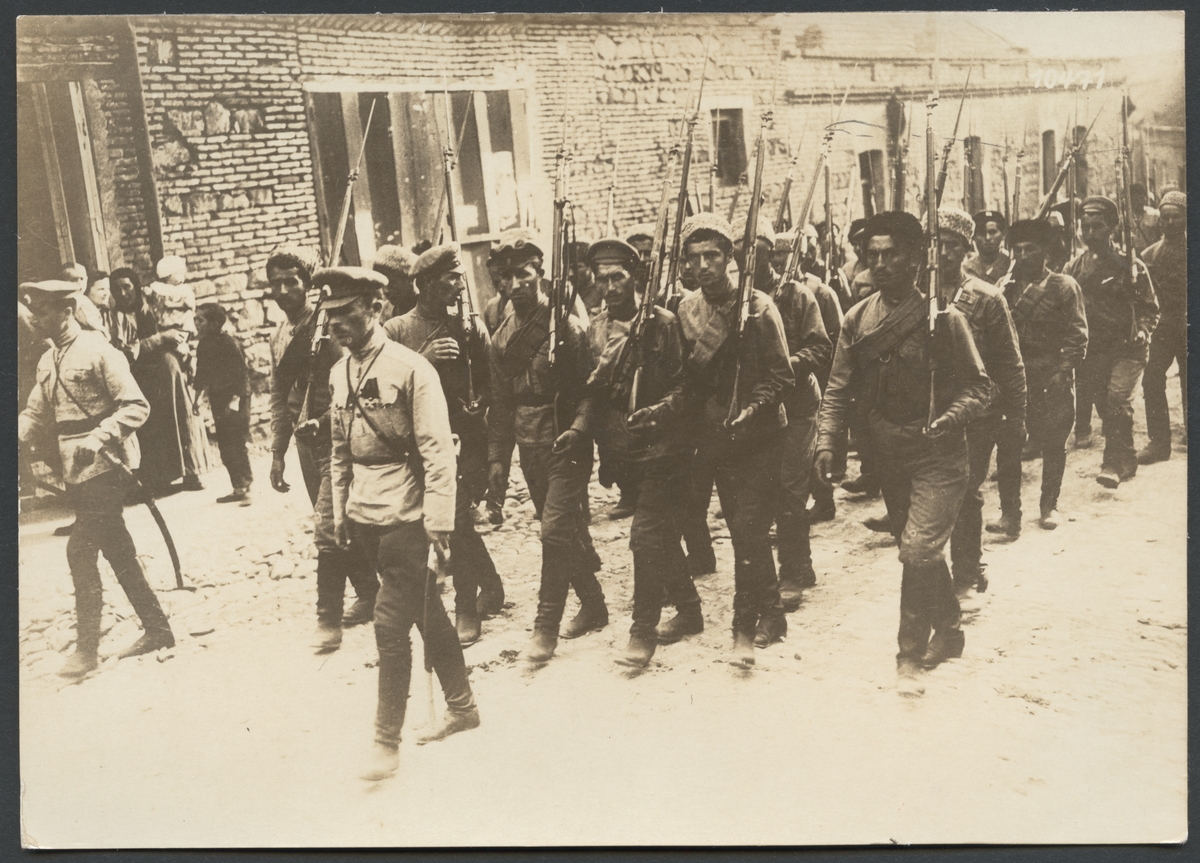 Bilden visar en tåg soldater som enligt påskrift på bilden delta i en begravningsceremonie.