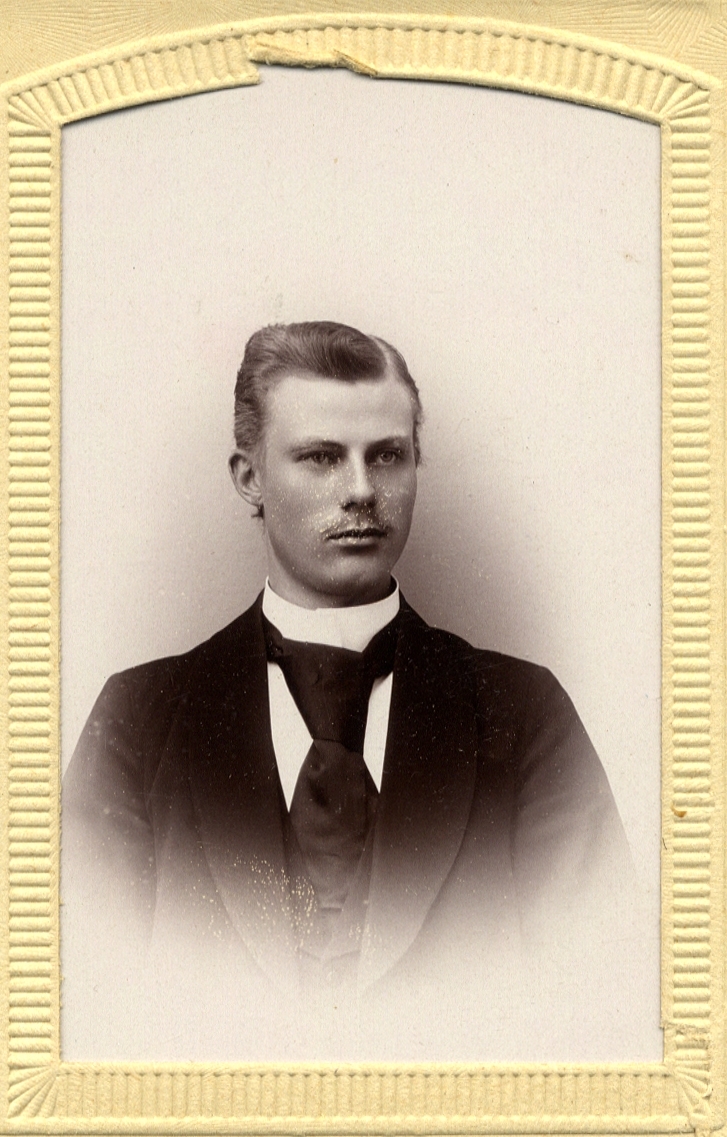 Foto av en ung man i mörk kostym med stärkkrage och slips. 
Bröstbild, halvprofil. Ateljéfoto.
