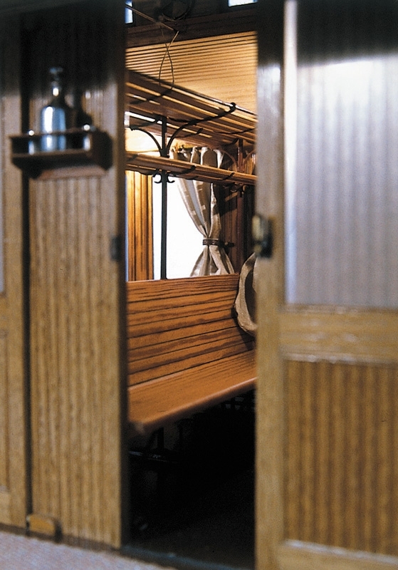 Modell av SJ 3:e klassvagn av rödbrun plåt, försedd med lanternin och grindar. Boggier. Grå gardiner i fönstren. Träinredning.

Skala 1:10,  Litt Co1 Nr 1054