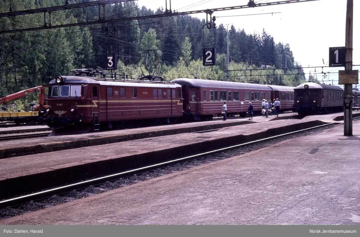 Elektrisk lokomotiv El 11 2102 med persontog fra Skien til Oslo på Hjuksebø stasjon. Bak til høyre styrevogn BFS65 med motorvogn BM65 med lokaltog til Notodden
