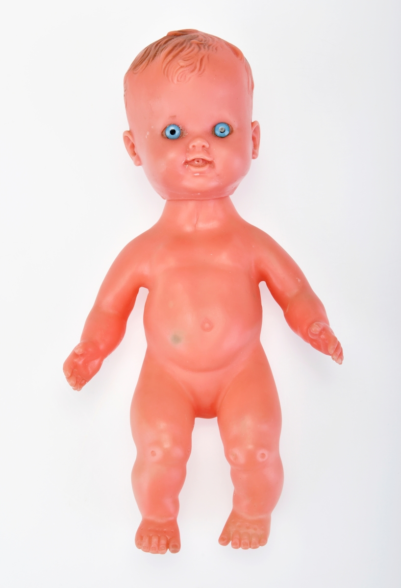 Dukken har støpt hår som er malt brunt. Den har blå øyne av plast. Ermer og ben er ikke leddet.