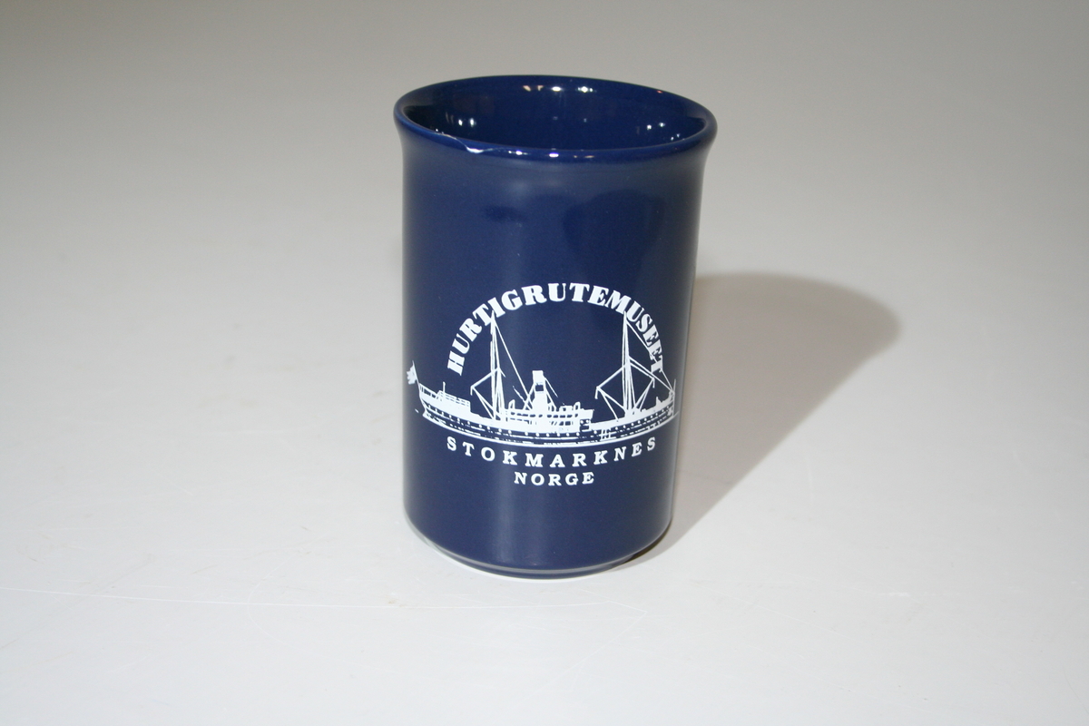 En blå kopp med hank. På koppsiden står logoen av Hurtigrutemuseet. Drikkekanten har en liten sprekk.
