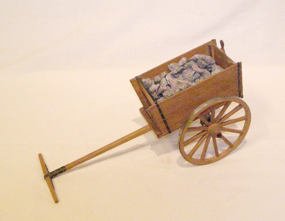 Modell i skala 1:10 av en storkärra. Kärran är gjord av trä, med en hjulaxel och bara två hjul. Den är lastad med grus som ska simulera småsten.