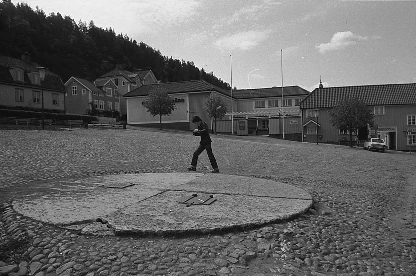Fotografi av brunnen på Gränna torg. En pojke passerar på dess andra sida.