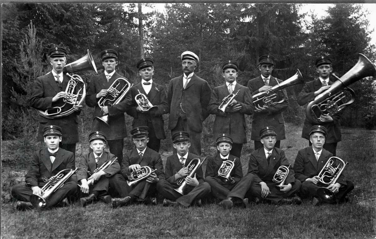 Et musikkorps, Glassverkmusikken, bestående av 14 menn er oppstilt med sine instrumenter.
