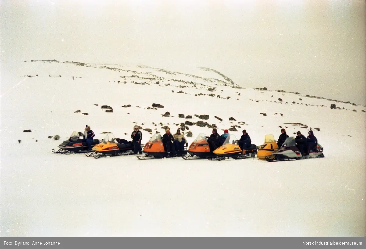 Gruppe med mennesker på fjelltur med snøskuter samlet på rekke og rad i fjellet