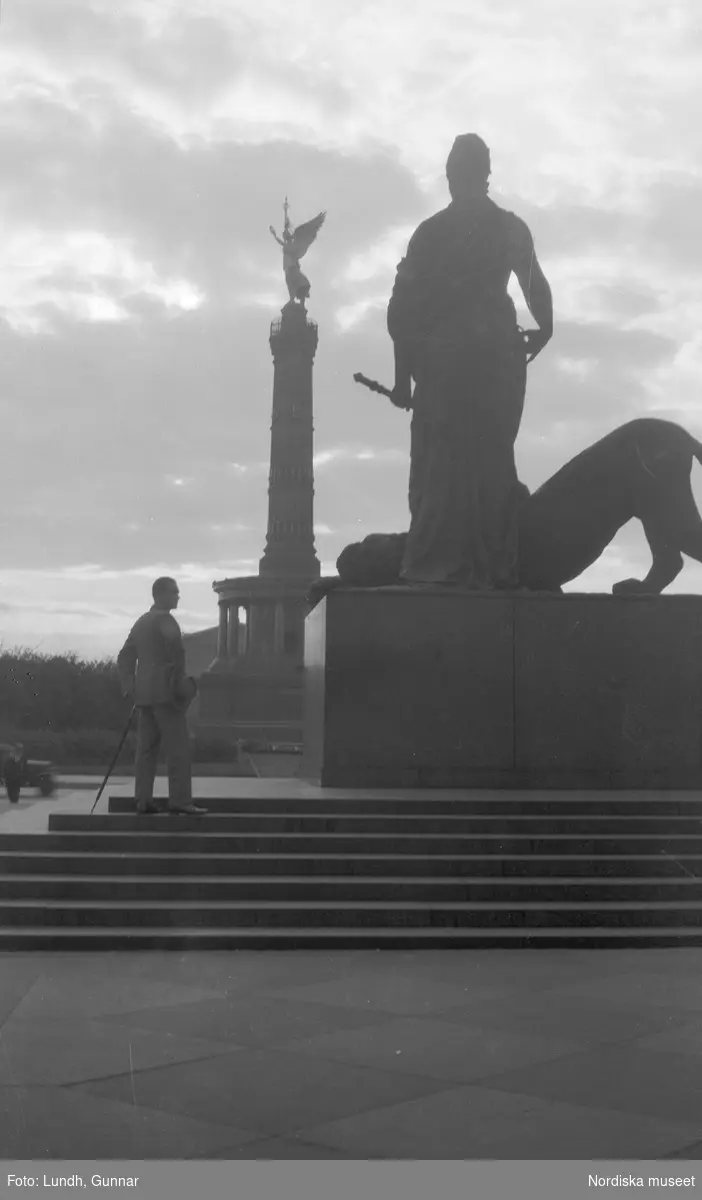 Motiv: Utlandet, Berlin 114 - 146 ;
Gatuvy med en kvinna och en man som går på en gata, anteckningar på kontaktkarta 139 "Monument vid Riksdagen, Berlin" 140 "Monument vid Siegessäule".