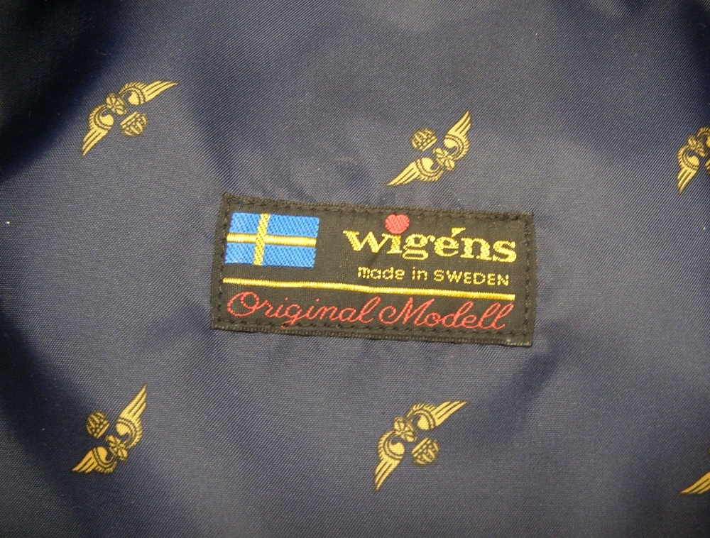 Skärmmössa med lågt kapell av vintertyg och mörkblått mössband.
Guldfärgad stormträns och mösstränsknappar (1991).
Stort mössmärke av 1991 års modell.