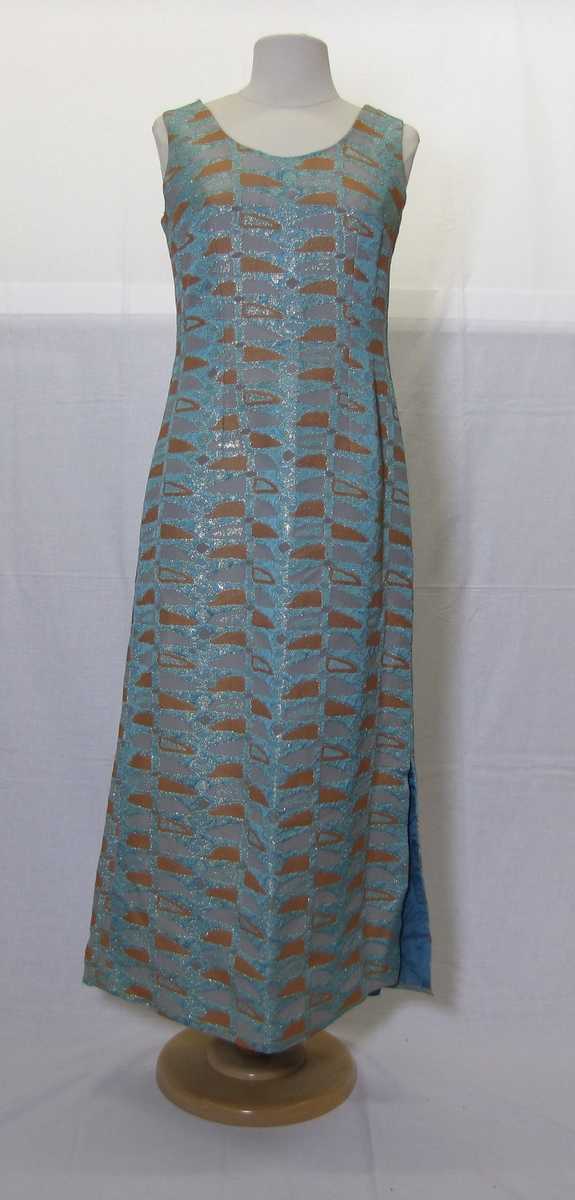 Ermeløs kjole med glidelås i ryggen og split på høyre side. Organisk og repeterende mønster vevet inn stoffet med grå, oransje og sølvtråd.