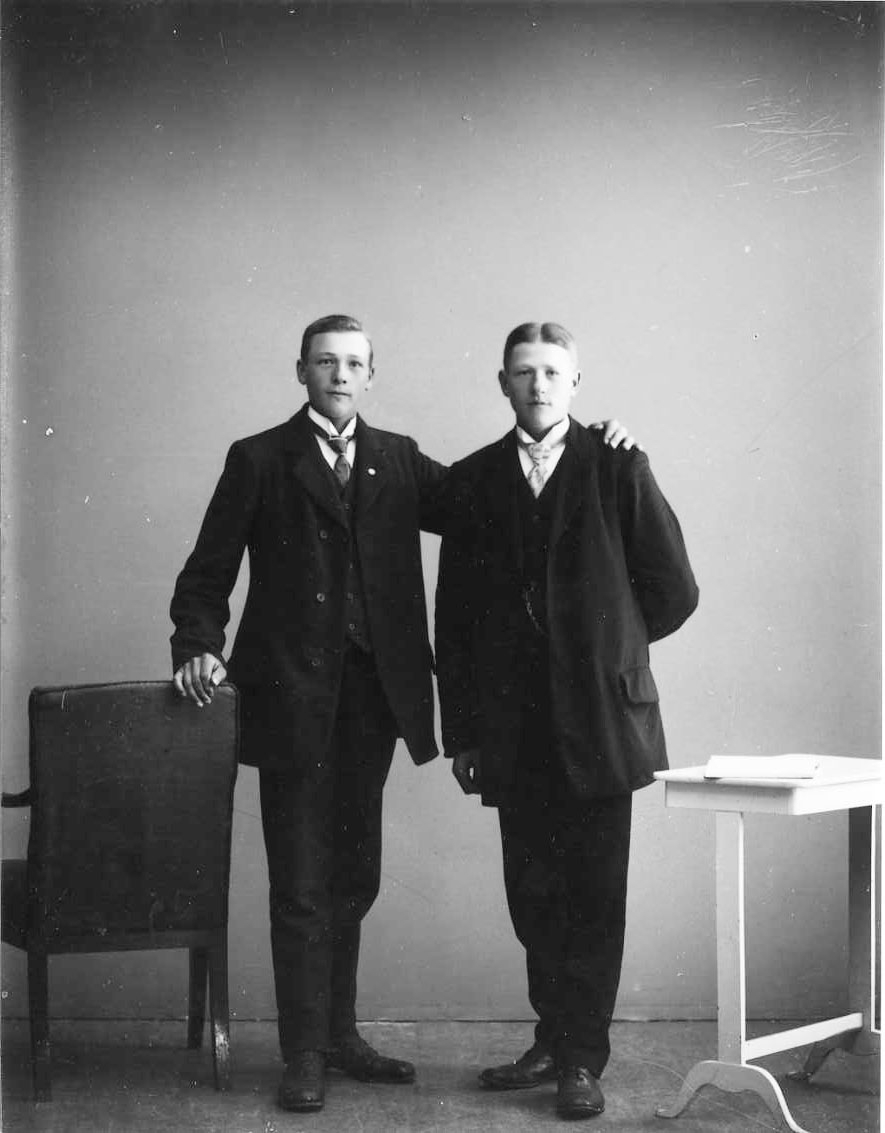 Gruppbild med två finklädda unga män. Den oidentifierade mannen till vänster håller vänster arm över axeln på Anton Lundkvist.