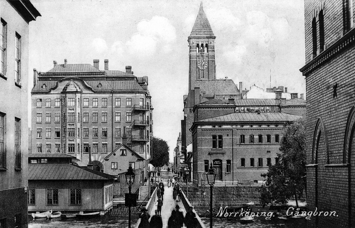 Vykort med motiv från Sandgatan i Norrköping. I bilden ses den nya spången anlagd 1926 efter skapandet av Strömsparken vid Revensgrund. I bakgrunden ses Rådhuset med Gull-Olle på sin tron överst på tornet. Där hitom på vänster sida av Nya Rådstugugatan ligger bankpalatset uppfört 1899-1902. Byggnaden till höger hitom Rådhuset är Varmbadhuset, Byggnaden vänster om bron är Klapphuset.