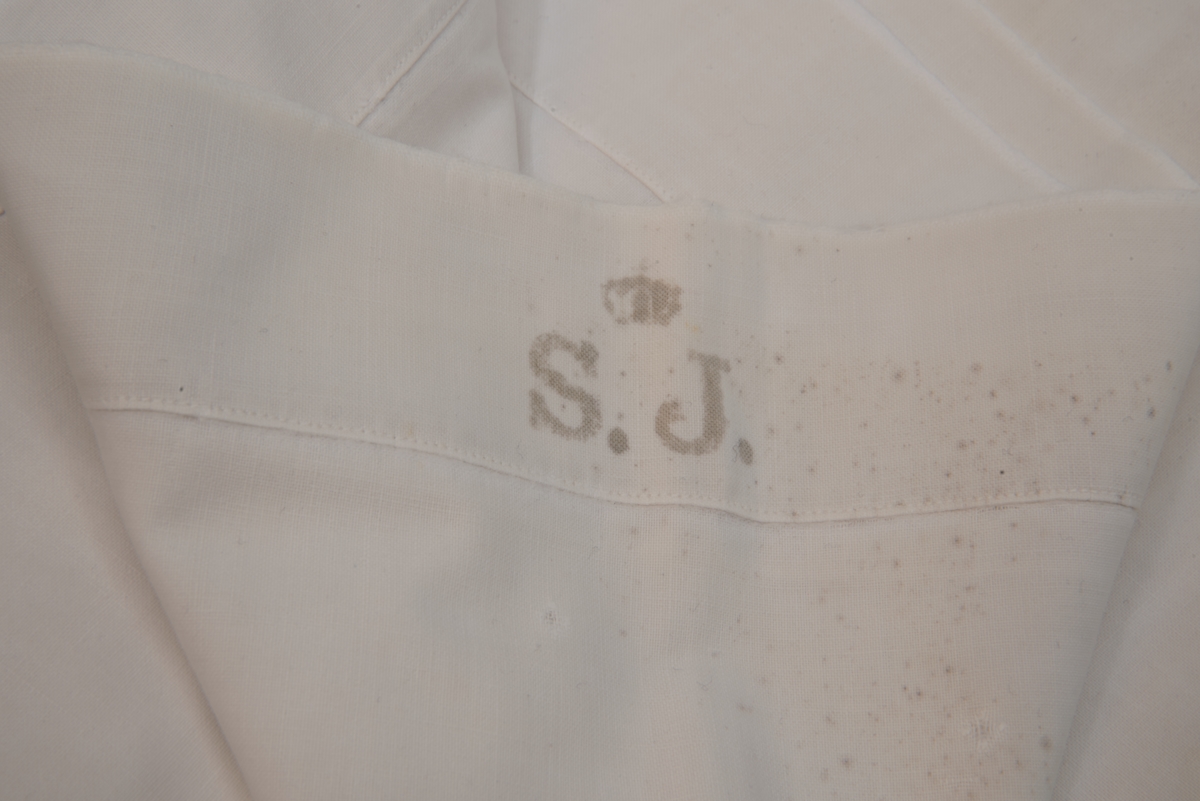 Påslakan, vitt med tryck "S.J." krönt av en kunglig krona. Påslakanet har flera lagningar.