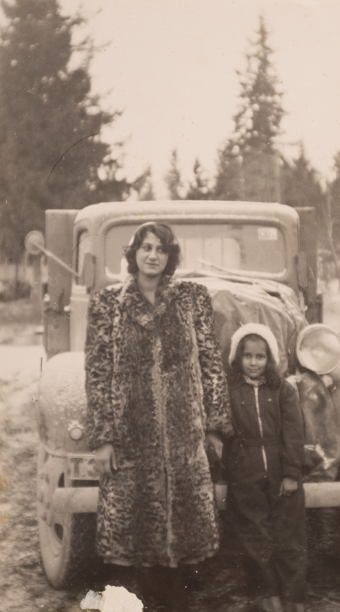 En ung romsk kvinna och en flicka framför en bil. Fotografiet är taget i Storvik 1947 i närheten av brandstationen.