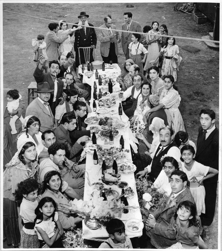 Stort romskt dubbelbröllop i Eskilstuna, troligen sommaren 1951. Långbordet är fyllt med mat, dryck  och smyckat med blommor. Många släktingar har samlats till festligheterna. Det ena av brudparen sitter på högra sidan av bordet.