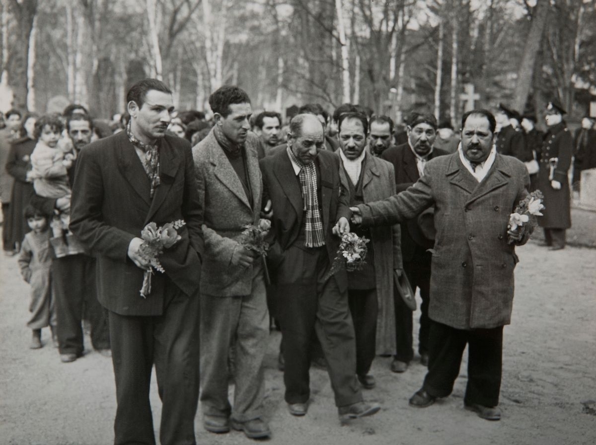 En stor grupp romer vandrar med blommor i händerna mot en begravning.