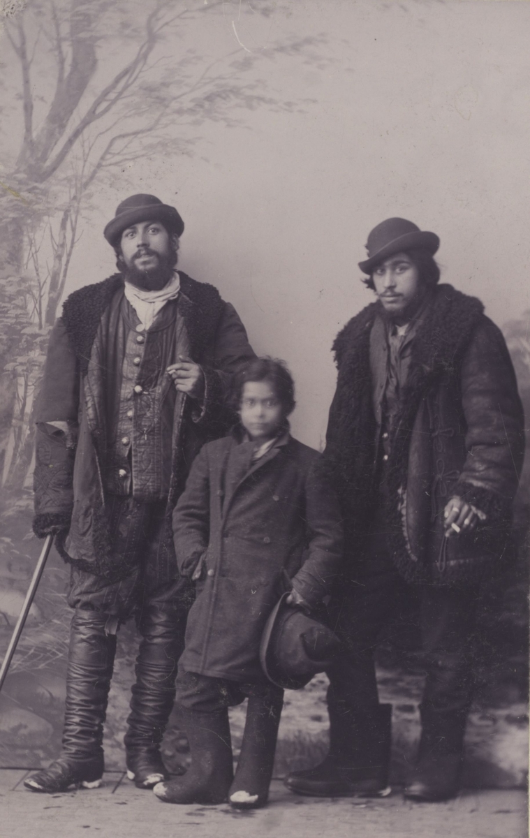Två män och ett barn har ställt upp sig för studiefotografering. De tillhör den grupp romer som folkvandrar genom Europa under 1800-talets andra hälft och kommer till Sverige via Ryssland och Finland. Fotografiet är taget i Tavastehus, Finland, och har troligen följt med familjen i bohaget.