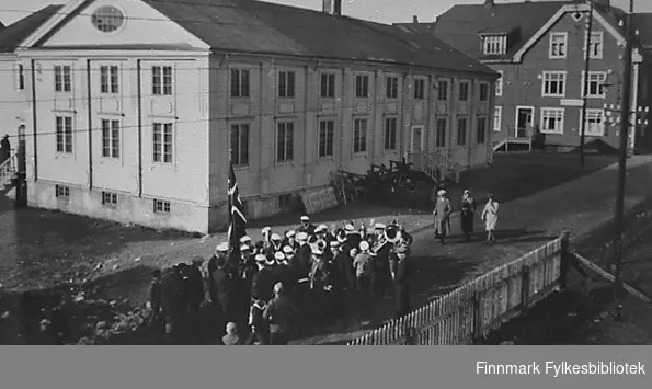 Kirkenes ungdomslag forsamlinghus, Malmklang, bygd i 1924. I forgrunnen står et musikkorps. I bakgrunnen står trygdekassen.