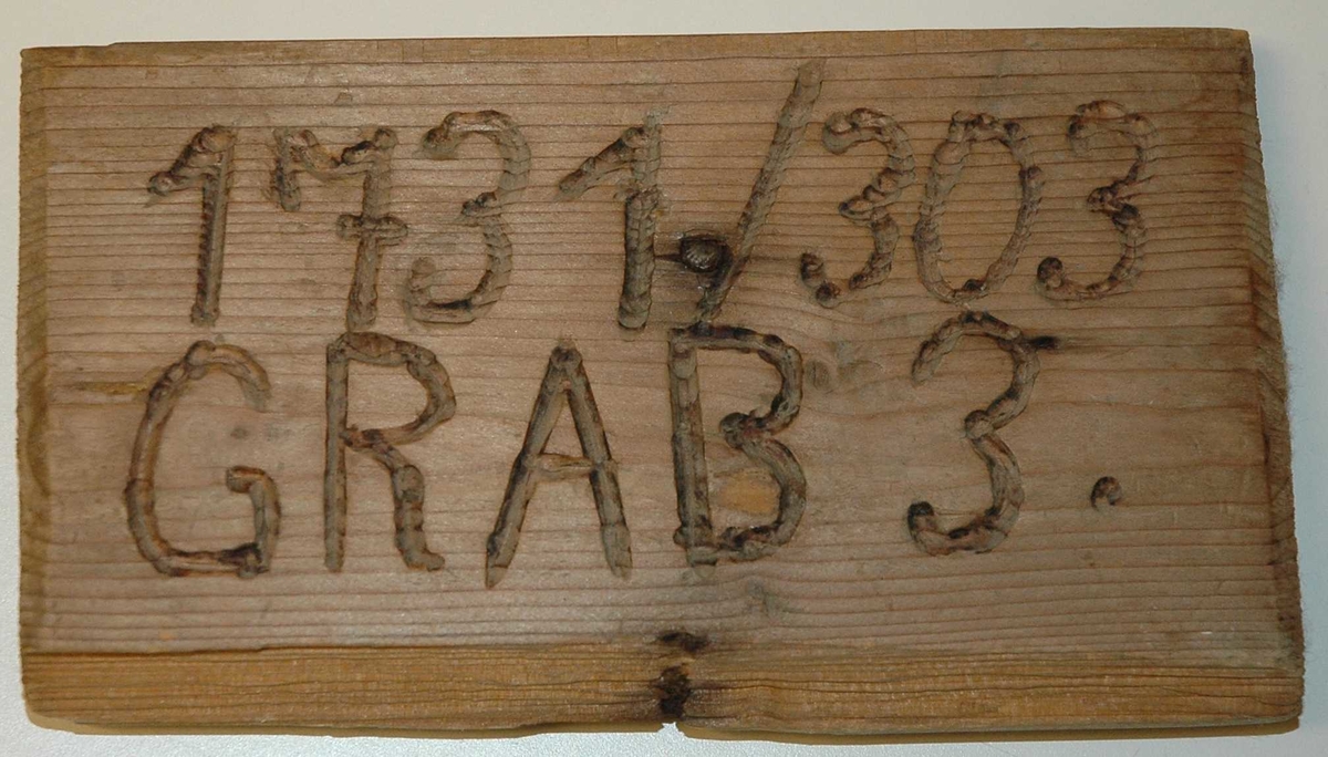 Trestykke med utskåret tekst "1731/303" "GRAB 3.". Gjennom trestykket er det slått en spiker. Sannsynligvis gravskilt, men ukjent hvor det har vært brukt. !1731/303" må trolig tolkes som fange 1731 fra Stalag 303 (Jørstadmoen), kanskje død i en arbeidsleir et annet sted i Norge.