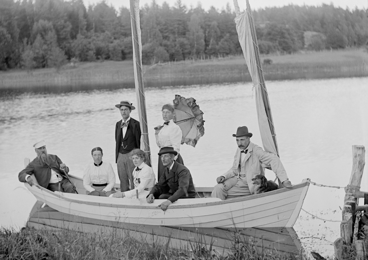 Fotograf Emil Durling med okänt sällskap i segelbåt intill bryggan vid Strömmen i Sankt Anna socken. Han ses sitta framför damen med paraply i hand.