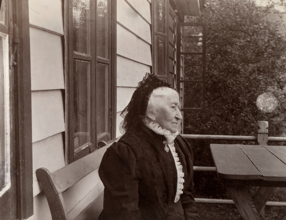 Portrettfotografi av ei eldre kvinne som sitter på en benk på verandaen.
