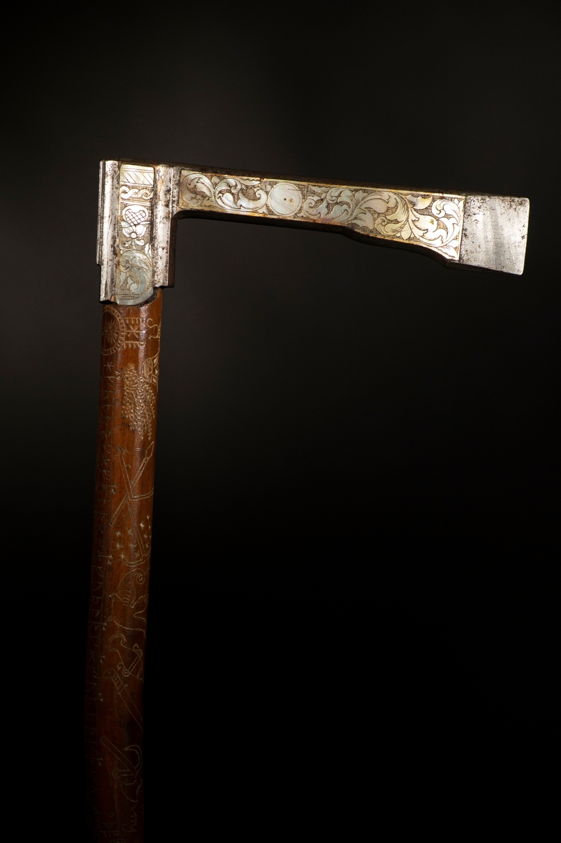 Av trä, med yxhuvud av pärlemorinlagd metall. Längs staven en runkalender med gyllental från och med 1795.
Mått: Yxa 135 mm.