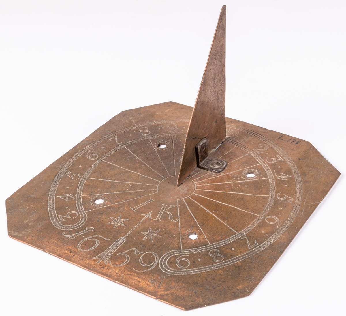 Solvisare av koppar, fyrsidig med triangulär stående visare. Fyra borrade hål för skruvar. Ristat cirklar med timsiffror och radiära linjer från centrum.  Märkt: "IK 1659".