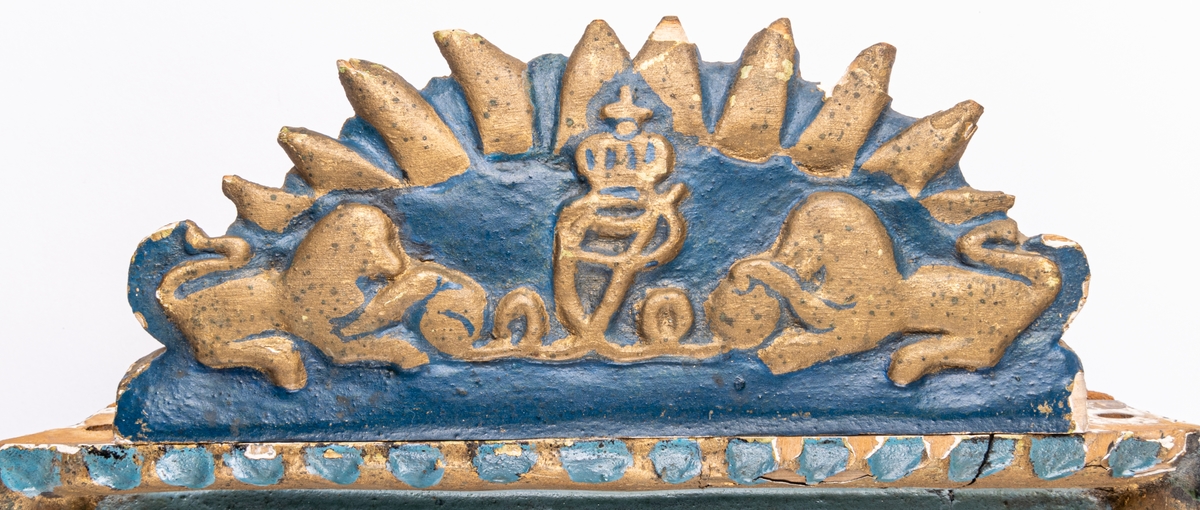 Klockfodral i skuret trä, blåmålat och förgyllt. Reliefbilder; krona, fiskar, delfiner, växtornament samt svårlästa bokstäver (Carl Johans namnschiffer?) samt märkt 1812. Runt hål i mitten.