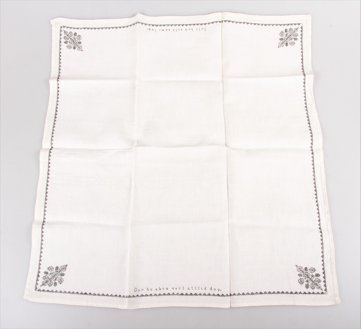 Bordduk med hvit bunn og med svart og hvit dekor. Brodert med korssting, kontursting og hullsøm, border og blomster samt tekst.
