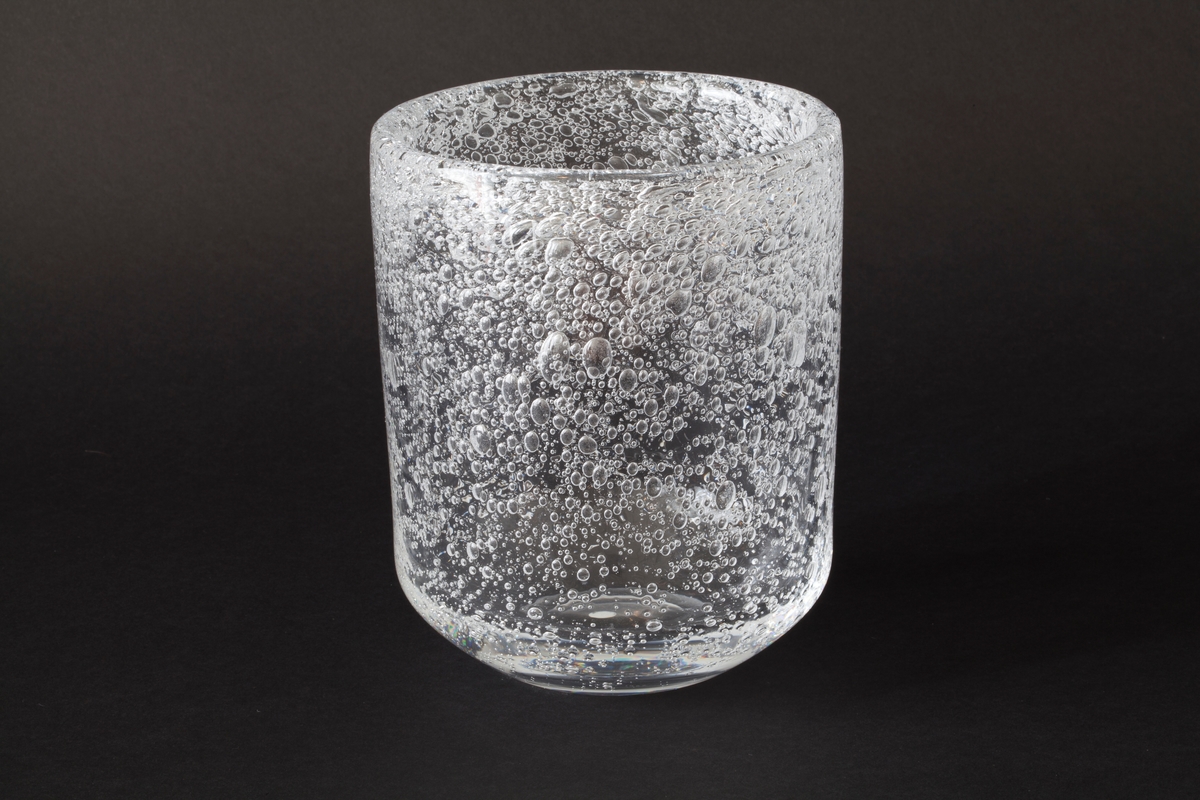 Tilnærmet sylinderformet vase i klart glass. Nedre del av korpus er konisk, og hviler på en sirkulær fotring. Øvre del avsluttes med en mykt avrundet kant. Hele vasen er dekorert med store og små sodablærer, som øker i tetthet på øvre del av korpus.
