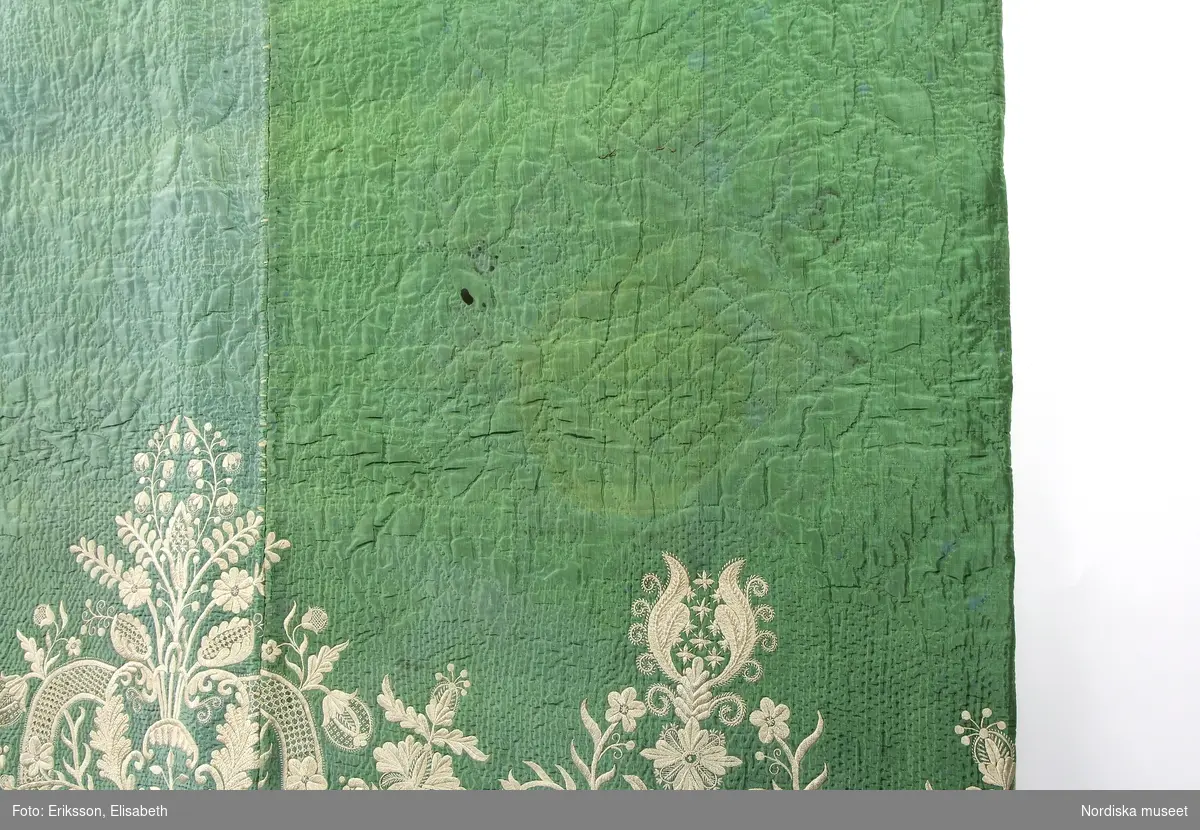 Katalogkort:
Stubb
av grön sidentaft sticksöm i blad-blom- och rutmönster. Nedtill bårdbroderi 44,5 cm.br. sytt i platt-stjälk-knut- och bottensöm med cremefärgat, rätt groft silke. Tunn vaddering. Foder av kyprad glättad beigefärgad bomull. Hopsydd på N. Museet