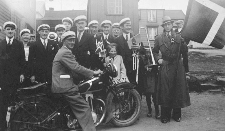 Vadsø Hornmusikk i 17.mai på 1930-tallet. Ivar Sælø sitter foran på motorsykkel. Det er også to barn med på bildet. Nesten alle personene er navngitt. 