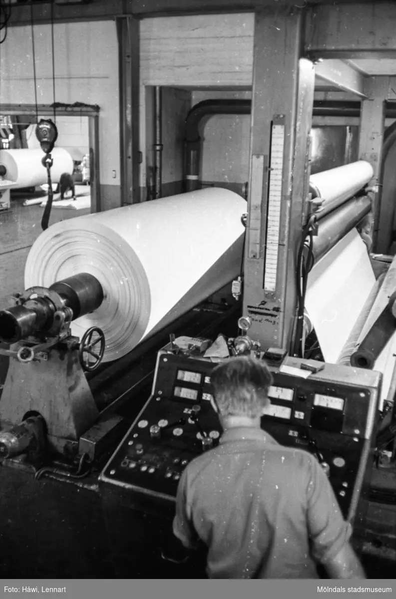 Mannen på bilden är arbetsledare Lars Elfström i arbete vid maskin, RM 5. I bakgrunden syns maskin Glätt 5. Pappersbruket Papyrus i Mölndal, hösten 1970.