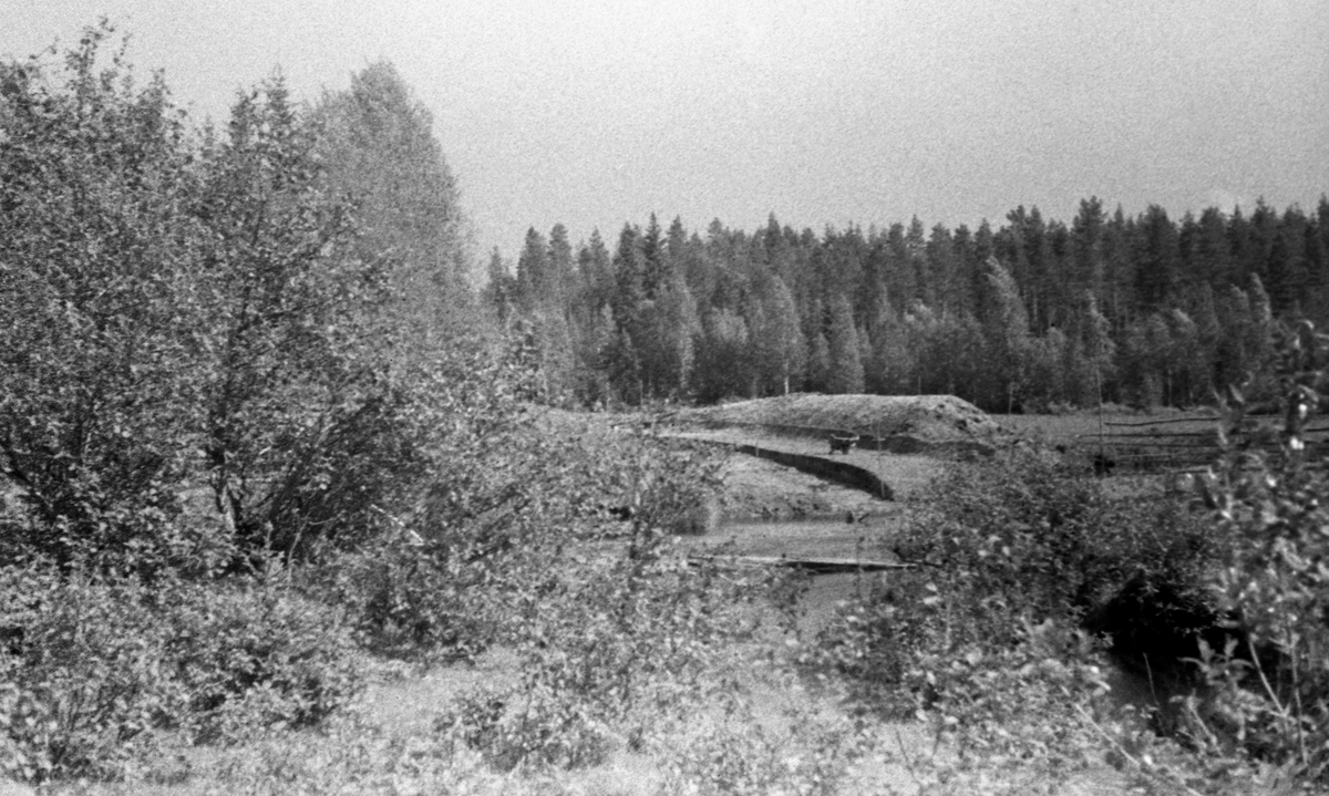 Bygging av fløtingsdam ved Lergravsrønningen i Agåa, et sidevassdrag til elva Jømna i søndre del av Elveum kommune i Hedmark.  Fotografiet er tatt fra ei bakkehelling med grasmark og bjørkekratt, mot vassdraget, hvor vi skimter ei trillebår mellom ei nedgravd grøft og en oppspadd jordvoll.  Til høyre for sistnevnte ser vi et våtmarksområde, som antakelig skulle brukes som reservoar for en attholdsdam.  Bildet skal være tatt i 1946. 

Agåa kommer fra Agsjøen øst for Agåsen.  Derfra flyter den først i nordvestlig, deretter i vestlig retning i 14-15 kilometer før den renner ut i elva Jømna, som er et sidevassdrag til Glomma.  Hele Agåa var i sin tid fløtbar.  Vassdraget hadde fire attholdsdammer, hvorav den avbildete på Lergravsrønningen var den nest nederste. 