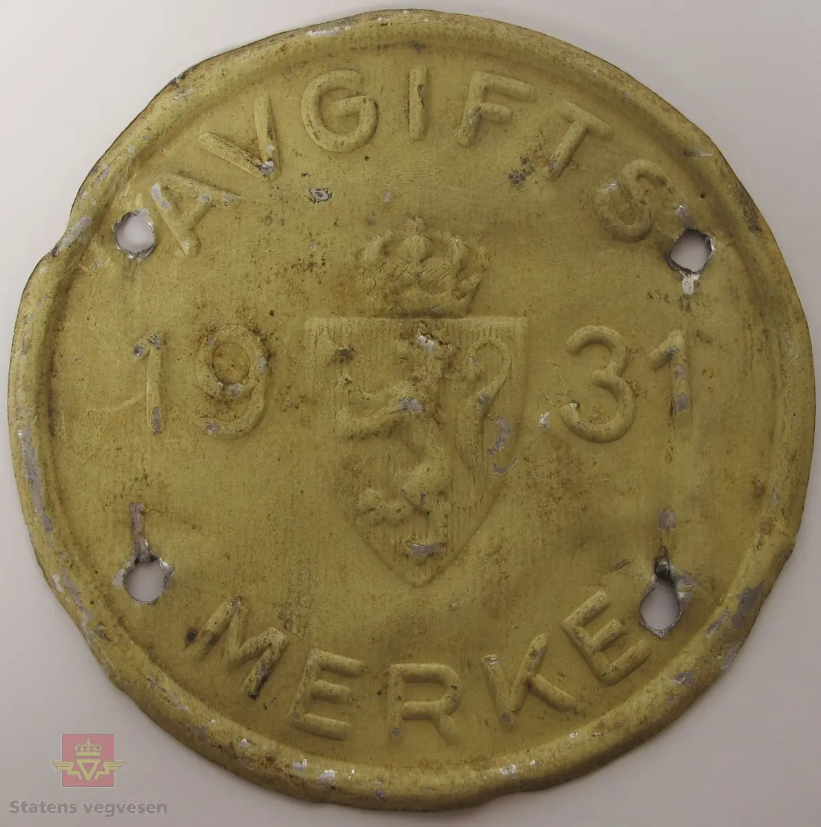 Rundt avgiftsmerke i gult med utstanset skrift og det norske riksvåpenet. Har teksten Avgiftsmerke 1931.