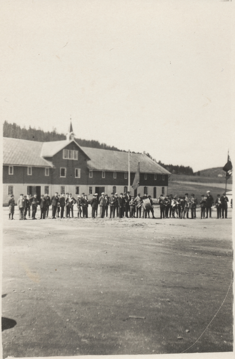 Folkemengde på gårdsplassen på Falstad skolehjem (Falstad nedre), før 1940. Flagg og instrumenter tyder på at det kan være 17. mai.