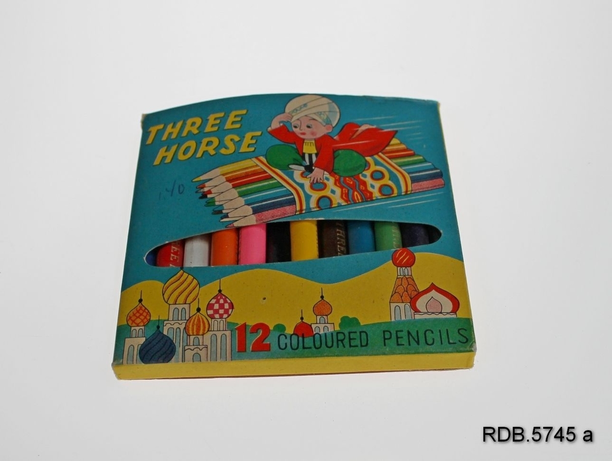 En pappeske med 12 fargeblyanter i tre, THREE HORSE. Tegning på eska av en gutt som bruker blyanter som flygende teppe. Det er en åpning i eska som du kan se blyantene gjennom.