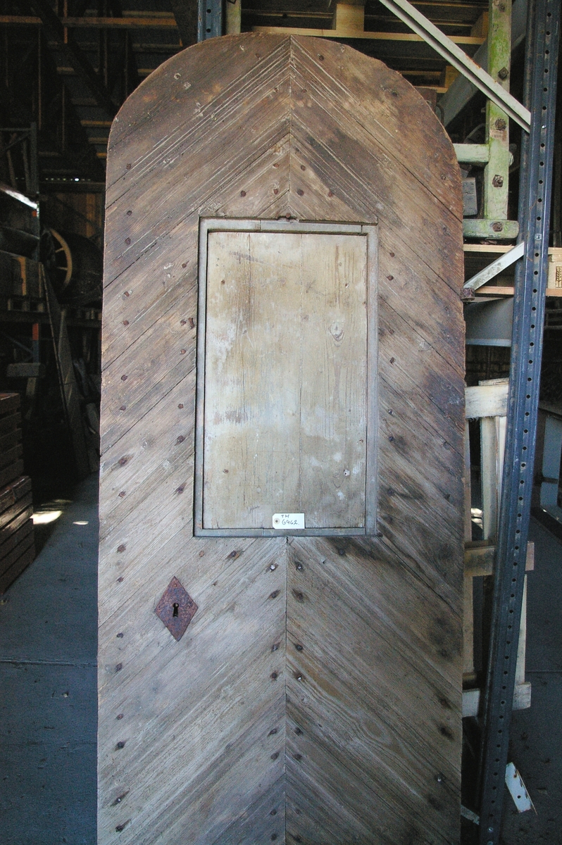 Døra er laget av 1 1/4 toms planker med to enkle drev som holder plankene sammen. Døra er belagt med profilert panel. Panelet er lagt på skrå i mønemønster og festet med spiker som har digre hoder. Døra har et vindu på 45 cm x 79 cm som innvendig er lukket med en liten hengslet dør. Døra er nærmest halvsirkelformet i toppen og passer da inn i buen i murverket. Låsen sitter på og har rombeformet nøkkelhullbeslag og to solide gangjern med to enkle knuter. Låsen sitter på innsida og er helt innebygd med jernplater og to slåtter. På innsida er rester etter påmalt marmorering.