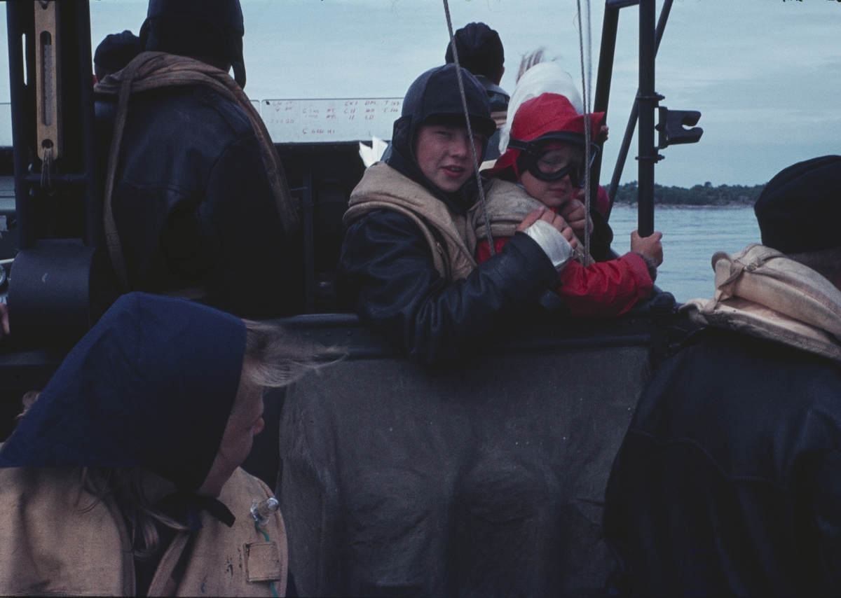 Bilden visar två barn i skyddskläder ombord på en motortorpedbåt.