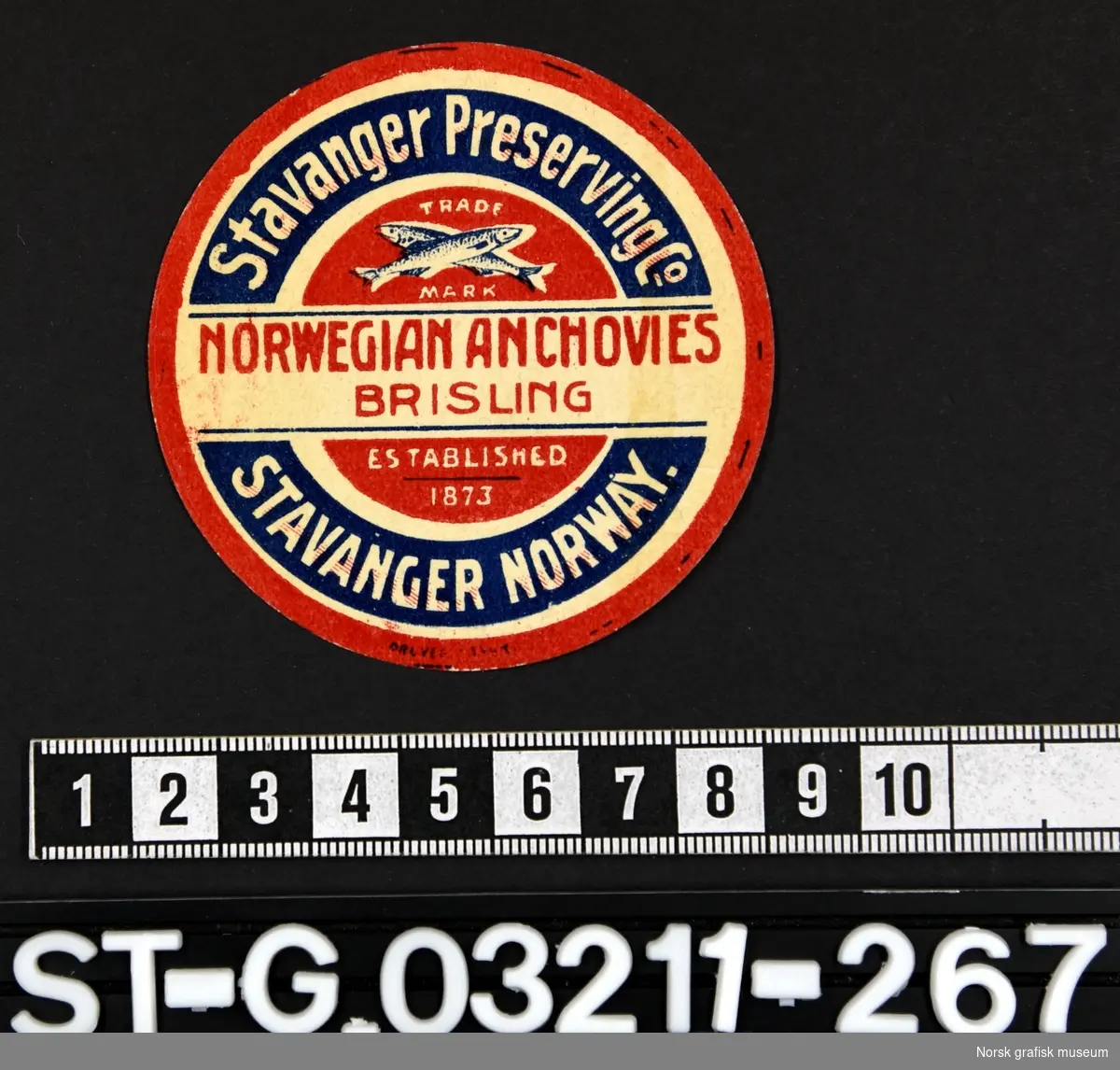Rund etikett i hvitt, rødt og blått. 

"Norwegian anchovies brisling"