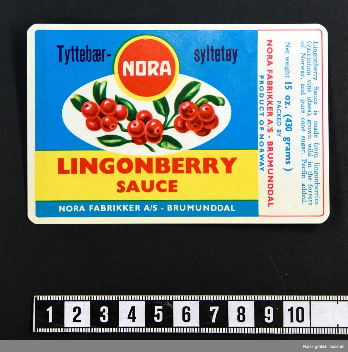 Etikett for tyttebærsyltetøy med blå bakgrunn, med en illustrasjon av tyttebær over varenavnet med rød tekst på gul bakgrunn.