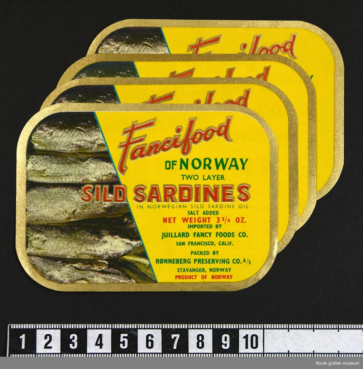Etiketter med gul brakgrunn, bord i gull og tekst i rødt og grønt. Venstre side viser innholdet i boksen, sardiner.

"Sild sardines in Norwegian sild sardine oil"