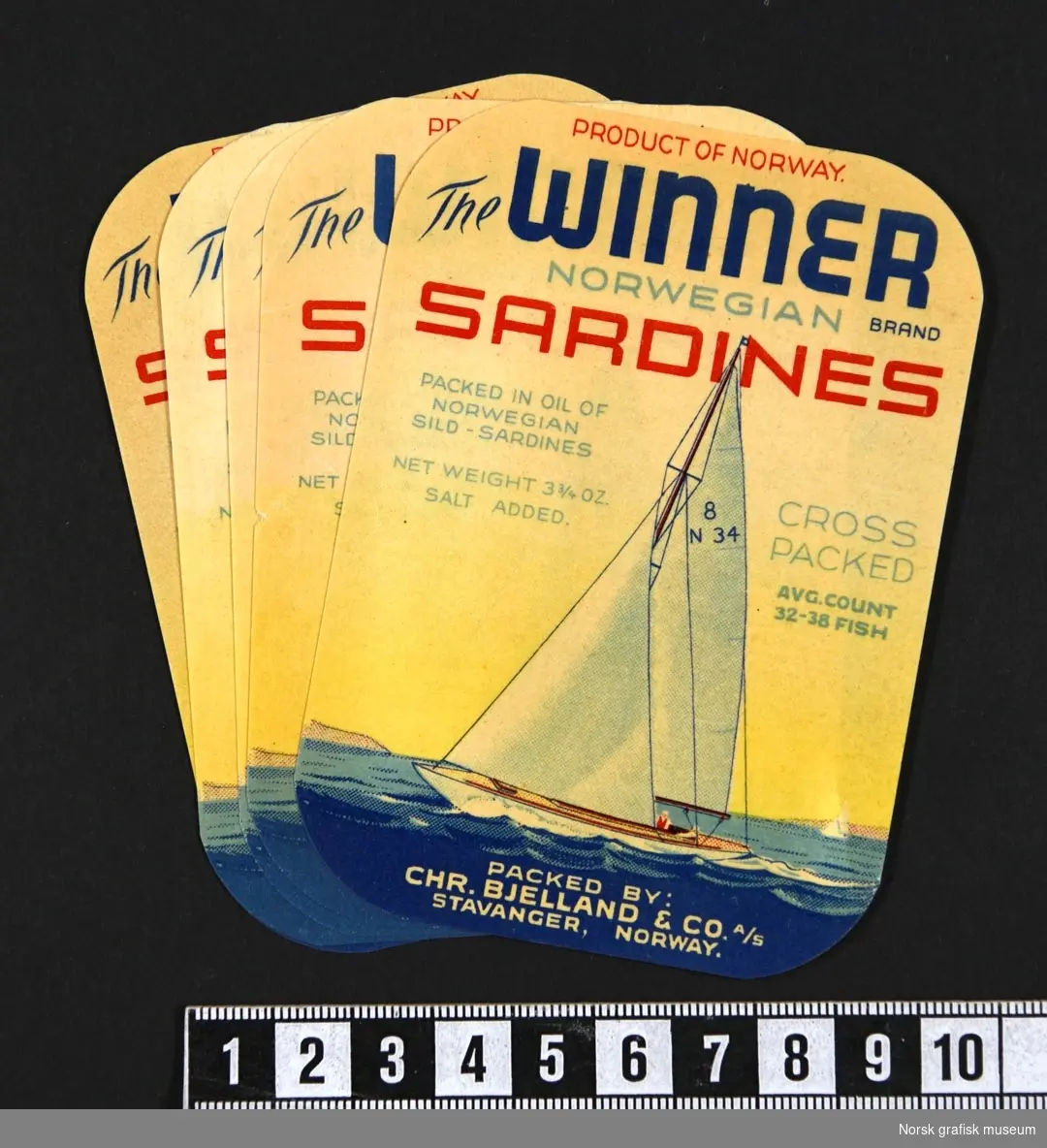Etiketter med fremstilling av en seilbåt med hvite seil, på blått hav, under en gul himmel. 

"Sardines packed in oil of Norwegian sild- sardines"